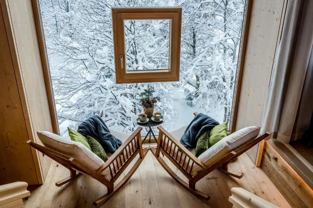 fauteuil à bascule devant la baie vitrée et le paysage enneigée depuis l'hôtel Werdenfelserei à Garmisch-Partenkirchen